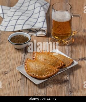 Empanadas di carne argentini con un bicchiere di birra su un tavolo di legno Foto Stock