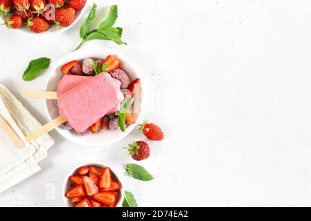 Il gelato alla fragola si apre su un piatto bianco su sfondo di pietra bianca con spazio libero per il testo. Vista dall'alto, disposizione piatta Foto Stock