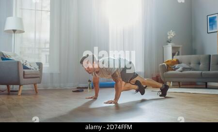 Muscular Athletic Fit Man in T-shirt e Shorts inizia energicamente Facendo Mountain climber esercizi a casa nella sua spaziosa e. Appartamento luminoso Foto Stock