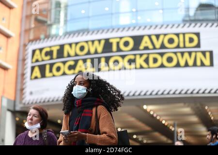 Una donna che indossa una maschera facciale cammina attraverso Manchester. Greater Manchester sarà sottoposta a controlli più severi sul coronavirus dopo gli ultimi colloqui con il primo ministro volti a garantire un ulteriore sostegno finanziario concluso senza un accordo. Foto Stock