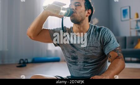 Felice e soddisfatto forte atletico Fit uomo in T-shirt e. Gli shorts sono acqua potabile dopo gli esercizi mattutini a Home in La sua vita spaziosa e luminosa Foto Stock