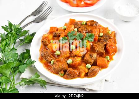 Stufato di manzo con patate e carote in salsa di pomodoro su piatto bianco, vista ravvicinata Foto Stock