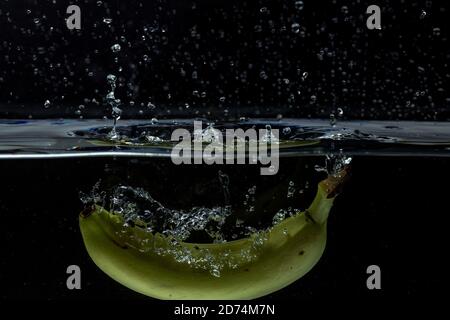 Primo piano vista della colorata banana gialla che cade in acqua su sfondo nero. Foto Stock