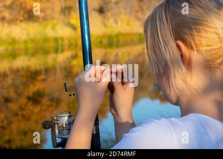 Giovane pescatrice si prepara a pescare. Mette l'esca viva (verme) sul gancio della canna da pesca con la bobina che gira. Primo piano, messa a fuoco selettiva. Foto Stock