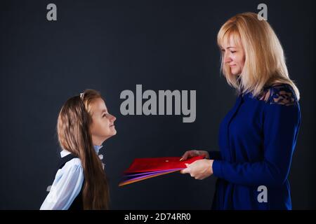 L'insegnante dà alla ragazza una cartella di studente con l'insegnamento materiale Foto Stock