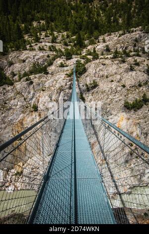 Ponte di legno lungo sopra la gola profonda con una spiaggia di fiume in fondo, tra le rocce. Montagne selvagge nelle Alpi svizzere Foto Stock
