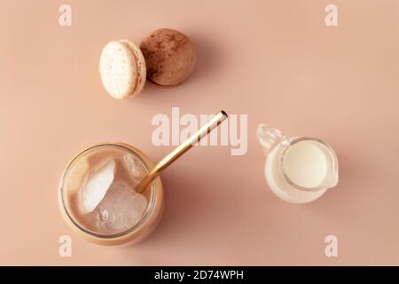 Bicchiere di caffè ghiacciato in vetro alto con paglia dorata con crema e macaroon cioccolato, vaniglia su sfondo pastello per il tuo design. Concetto di cibo in stile vintage. Stile di posa piatto. Spazio di copia. Primo piano. Foto Stock