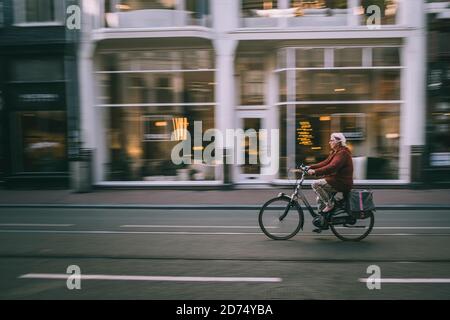 Donna in bicicletta per le stradine strette di Amsterdam durante i primi spostamenti mattutini. Paesi Bassi Foto Stock