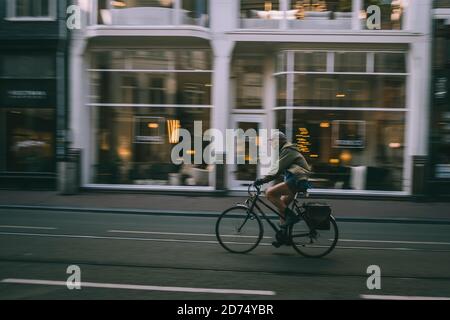 L'uomo anziano pedalando ad Amsterdam attraverso le stradine strette di fronte ad un negozio di mobili. Paesi Bassi Foto Stock