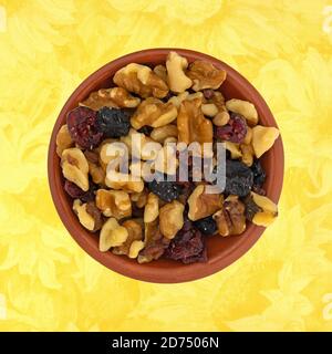 Vista dall'alto di una porzione di noci e frutta secca si mescola in una piccola ciotola di argilla su una tovaglia con motivi floreali gialli. Foto Stock