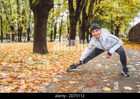 Donna atletica sorridente che fa un allenamento prima di fare jogging in un parco cittadino autunnale sul parco giochi per bambini Foto Stock