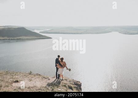 Lo sposo e la sposa si trovano su una scogliera di fronte di un grande serbatoio in distanza sono isole Foto Stock