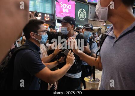 Un manifestante pro-Pechino che indossa una maschera è visto essere scortato da funzionari di polizia mentre affronta l'attivista pro-democrazia Joshua Wong durante la manifestazione.gli attivisti pro-democrazia di Hong Kong hanno avviato una campagna di social media a sostegno dei dodici giovani manifestanti presumibilmente incarcerati sulla terraferma dopo un fallito tentativo di fuga A Taiwan in motoscafo. I sostenitori sono incoraggiati a scattare foto del mare attraverso un segno trasparente e a caricarle sui social media con l'hashtag ''SAVE12'. Foto Stock