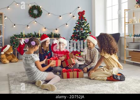 Gruppo di bambini amici scambiano regali il giorno di Natale seduto in soggiorno. Foto Stock