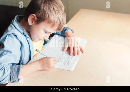 Primo piano del ragazzo carino che fa i suoi compiti. Capretto che scrive le linee differenti con la matita. Concetto di educazione dei bambini. Foto Stock