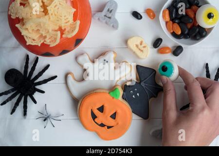 La mano della donna che tiene un occhio di Halloween, sul tavolo con altri ossequi di Halloween Foto Stock