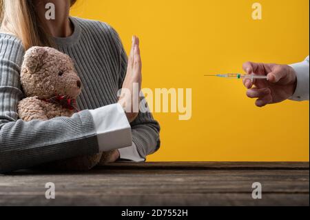 Donna che fa un gesto di arresto verso un ago di vaccinazione mentre protegge il suo orsacchiotto in un'immagine concettuale del movimento anti-vaccino. Foto Stock