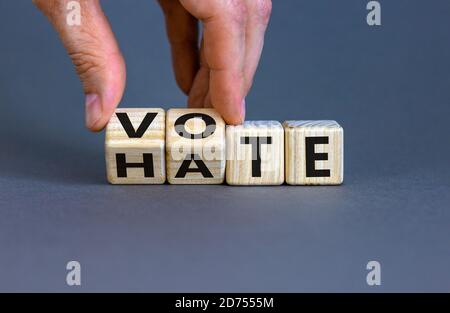 La mano gira i cubetti di legno e cambia le parole 'Vota' in 'odio' o viceversa. Splendido sfondo grigio, spazio per la copia. Concetto. Foto Stock