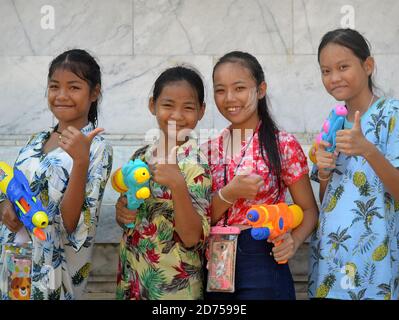 Quattro ragazze pre-teen di Bangkok trasportano le pistole dell'acqua di plastica, danno i pollici-in su il gesto e il sorriso per la macchina fotografica durante il festival dell'acqua di primavera di Songkran. Foto Stock