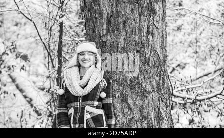 donna sorridente vicino all'albero. festa invernale giorno. donna carina in abiti caldi. Godersi la natura wintertime. Ritratto di donna eccitata in inverno. Ragazza allegra all'aperto relax. Giacca a scacchi donna. Foto Stock