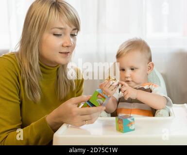 Una madre con un bambino piccolo è interessata a mettere insieme un'immagine dei cubi. Puzzle. Educazione domestica e cura dello sviluppo Foto Stock