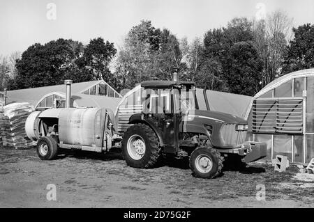 Un trattore agricolo John Deere che traina un rimorchio per irroratrici Pul-Blast è parcheggiato di fronte a diverse serre in un'azienda del New Hampshire. Caduta fogliame è in Th Foto Stock