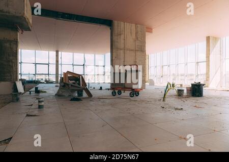 Cantiere di un centro commerciale all'interno. Accessori di costruzione, carrelli, vernice, fili elettrici, pavimento incompiuto all'interno di un edificio sotto i contro Foto Stock