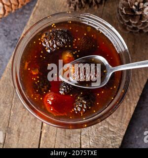 I giovani coni di pino si inceppano in una ciotola di vetro su tavola di legno. Deliziosa marmellata con i piccoli coni di pino. Foto Stock