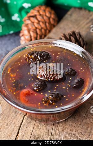 I giovani coni di pino si inceppano in una ciotola di vetro su tavola di legno. Deliziosa marmellata con i piccoli coni di pino. Foto Stock