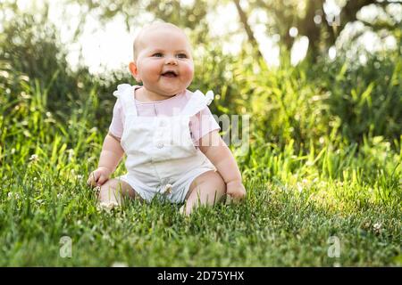 Felice adorabile bambina chubby seduta sull'erba Foto Stock