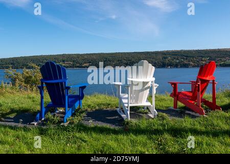 Tre sedie adirondack una rossa, blu e bianca siede sul bordo dell'oceano in una giornata di sole estate. Foto Stock