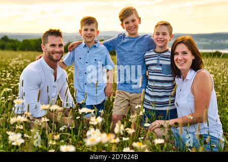 Felice famiglia su Daisy Field al tramonto che ha grande tempo insieme Foto Stock
