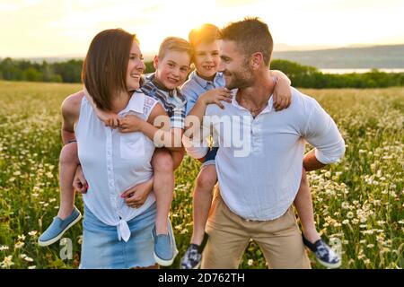 Felice famiglia su Daisy Field al tramonto che ha grande tempo insieme Foto Stock