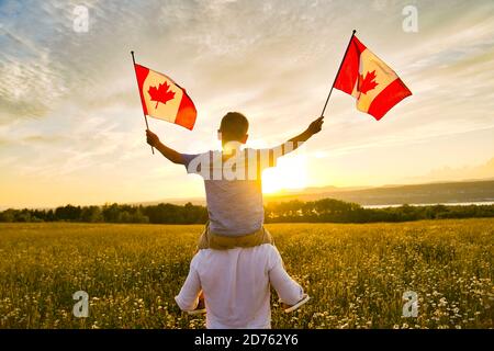 Adorabile ragazzo caucasico felice carino che tiene bandiera canadese sul spalla del padre Foto Stock