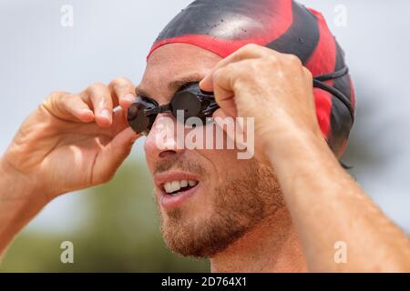 Triathlon atleta nuotatore in corso. Nuotatore triatleta maschile che mette occhiali da bagno pronti per una nuotata nell'oceano. Fit uomo in professionista Foto Stock