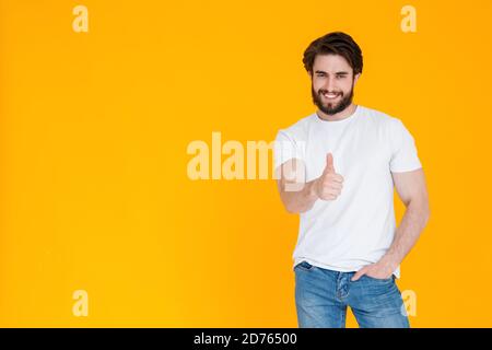 un giovane con un bell'osso in una t-shirt bianca e pantaloni in denim blu sorride alla telecamera e mostra un gesto simile. il linguaggio del corpo si alleva su Foto Stock