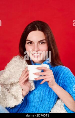 una ragazza in un pullover blu tiene una tazza di tè nelle sue mani. Foto Stock