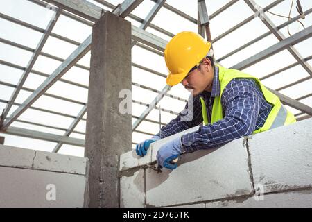 muratore a muratore che lavora con blocchi di calcestruzzo cellulare autoclavati. Walling, installazione di mattoni in cantiere Foto Stock