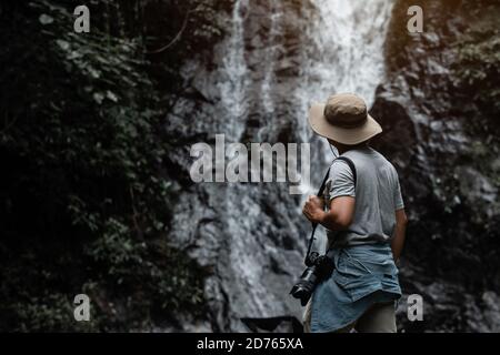 Viaggio asiatico maschile turista o fotografo fare un viaggio fotografico a una cascata nella natura, Bangkok, Thailandia in vacanza Foto Stock