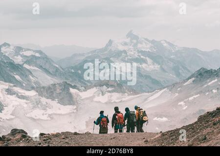 Estrema ricreazione e turismo di montagna. Un gruppo di escursionisti giù per il sentiero di montagna oltre l'orizzonte. Sullo sfondo, grandi montagne innevate. Co Foto Stock