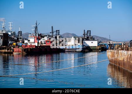 Navi industriali e barche ormeggiate nel vecchio porto di Drapetsona Pireo Grecia, cielo blu e mare, giorno di sole. Foto Stock