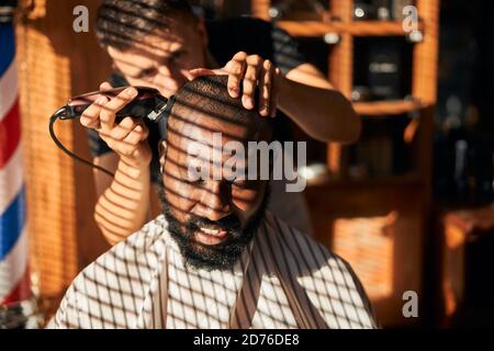 Sorridente Afro americano giovane uomo ottenere capelli tagliati in barbershop Foto Stock