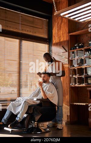 Barbiere maschio con bearded che taglia i capelli del cliente con le forbici Foto Stock