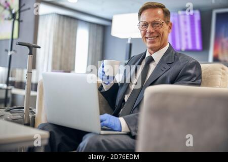 Felice uomo maturo che si rilassa con un computer portatile prima del volo Foto Stock