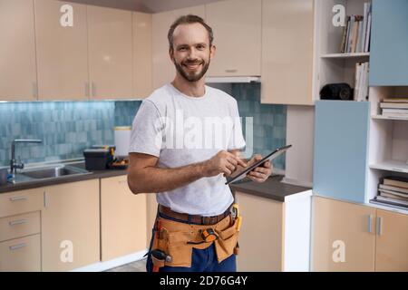 Sorridente giovane operaio caucasico con tavoletta durante il lavoro cucina Foto Stock