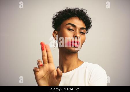 Uomo androgino che mostra le dita dopo aver strisciato il proprio rossetto . Uomo transgender con rossetto che guarda la fotocamera. Foto Stock