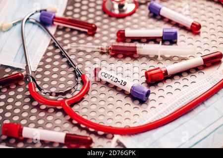 Analisi del sangue del concetto di covid-19. Campione di sangue, stetoscopio, siringa e maschera protettiva su fondo metallico Foto Stock