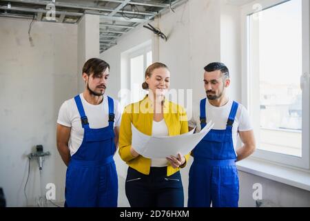 Una donna con un programma della casa nelle sue mani è parlare con due costruttori in tute Foto Stock