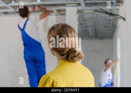 Una cliente femminile esamina il lavoro di un riparatore. Si alza con la schiena alla fotocamera Foto Stock