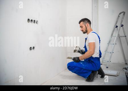 Un costruttore in tute usa una cazzuola per coprire il muro con cemento Foto Stock